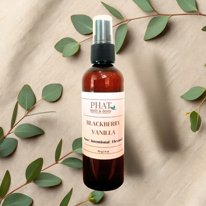 An amber spray bottle labeled PHAT Bath & Body Blackberry Vanilla, styled on a beige fabric background with eucalyptus leaves.