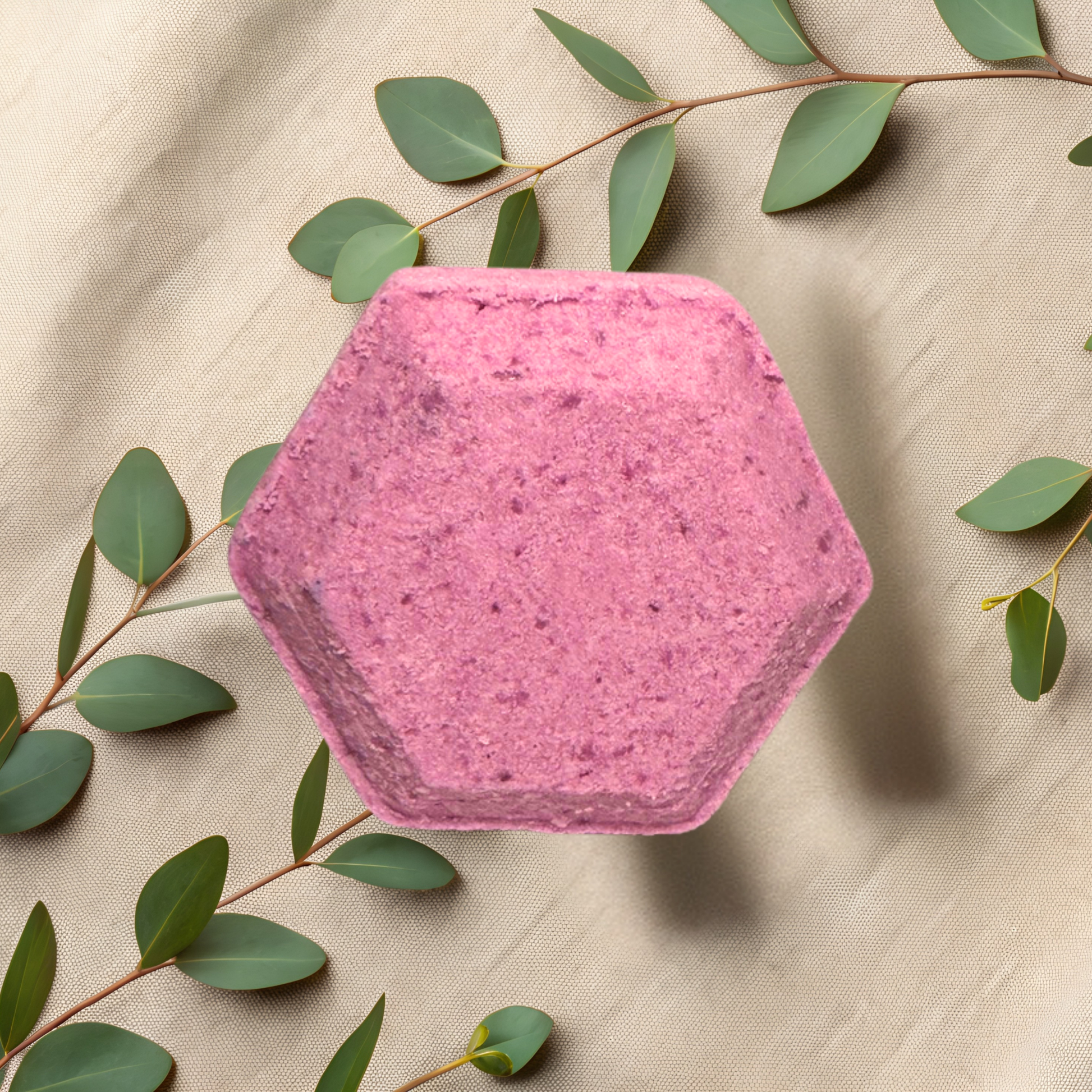Hexagonal pink shower bomb with green leaves on a beige fabric background