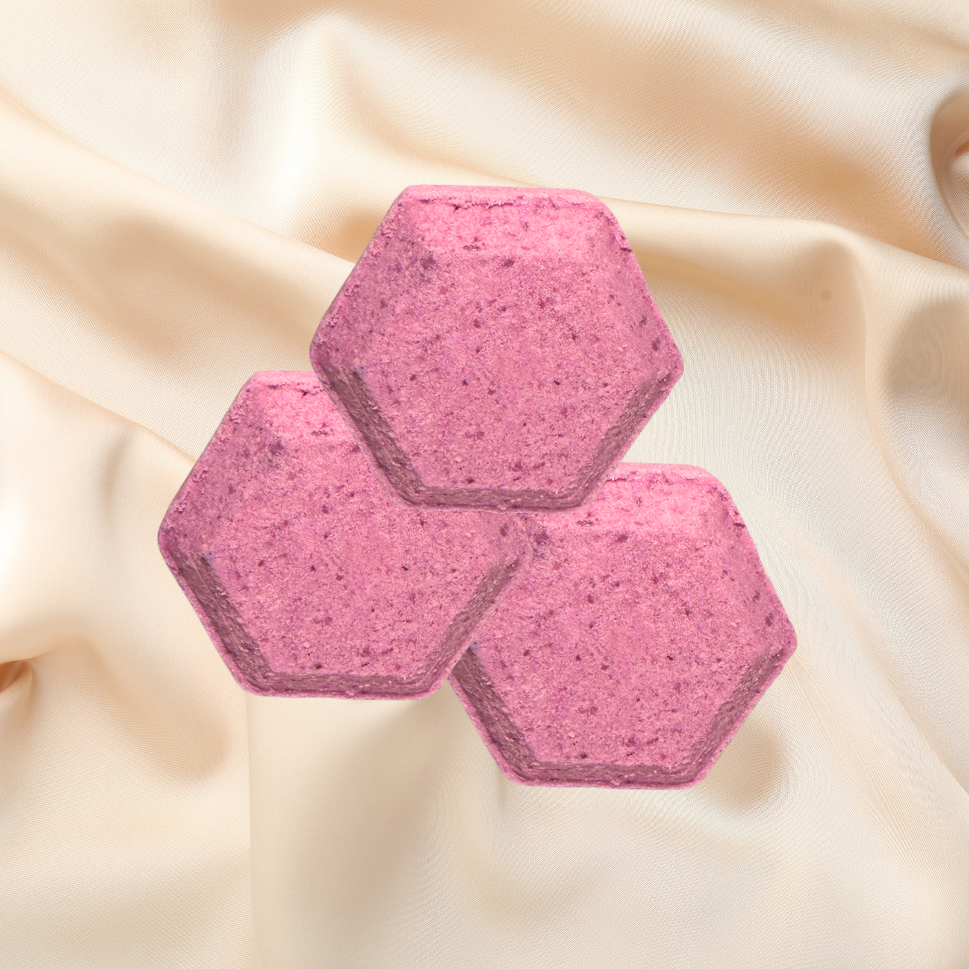 Three pink hexagonal shower bombs on a beige fabric background