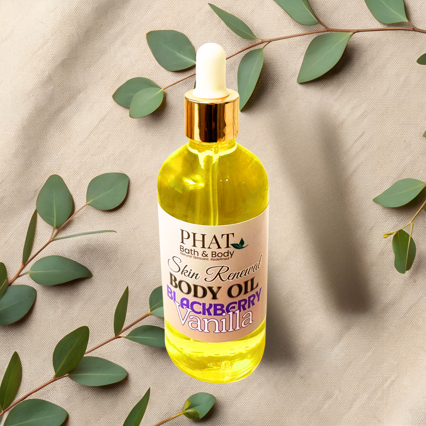 Bottle of Phat Bath & Body Skin Renewal Body Oil with blackberry vanilla scent on a beige fabric background with green leaves.