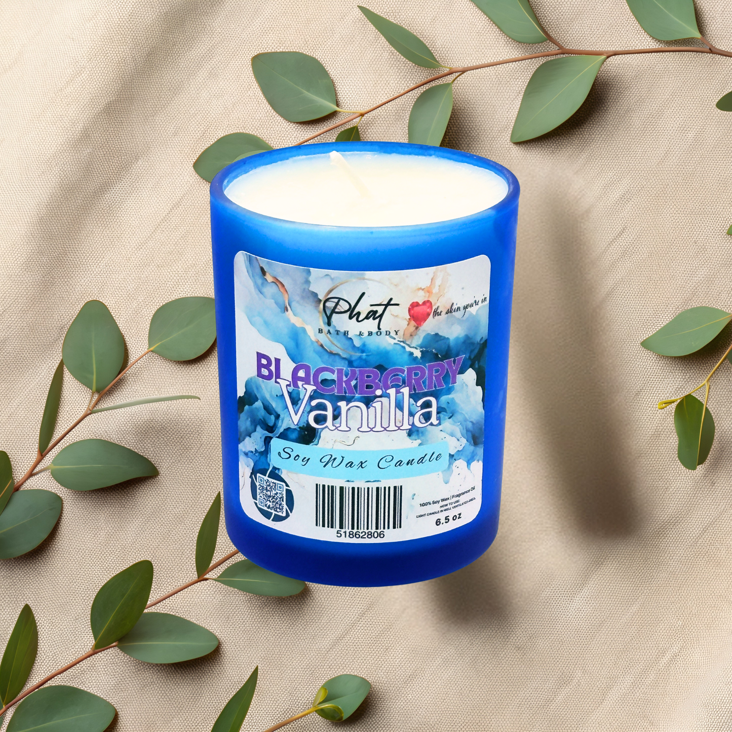 Blue candle with a label on a beige fabric background with green leaves