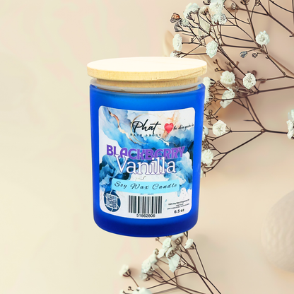 Blue candle with a wooden lid labeled 'Blackberry Vanilla' on a beige background with white flowers.