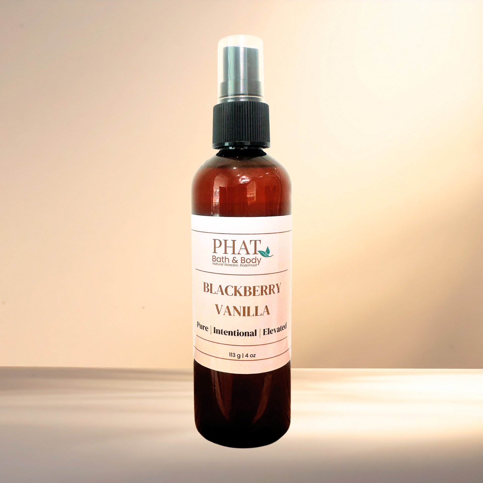 An amber spray bottle of PHAT Bath & Body Blackberry Vanilla body spray, featuring a white label and a black spray nozzle, set against a warm beige gradient background.