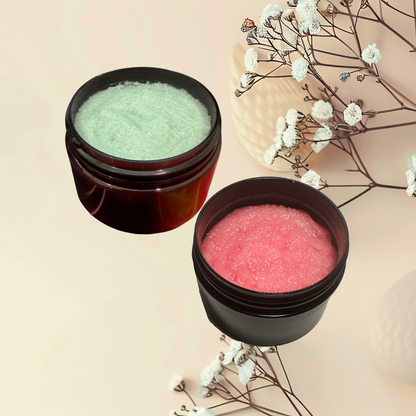 Two jars of facial scrubs, one green and one pink, on a light background with flowers.