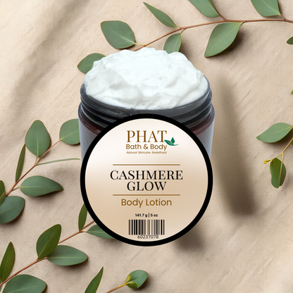 Jar of 'Cashmere Glow' body lotion from Phat Bath & Body on a beige fabric background with green leaves.