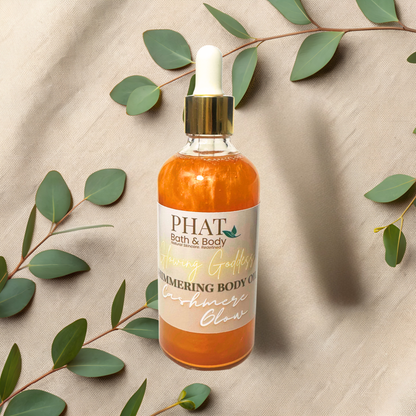 Bottle of 'PHAT Bath & Body' shimmering body oil with green leaves on a beige fabric background