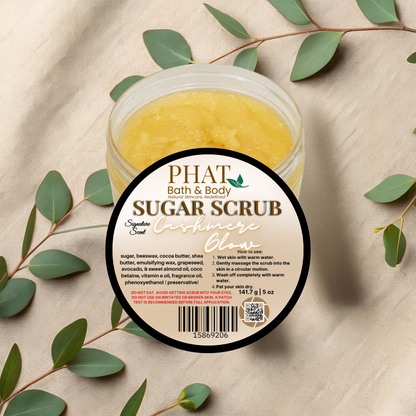 Jar of sugar scrub with a label on a beige fabric background with green leaves.