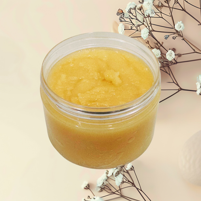 Jar of yellow sugar scrub on a light pink background with white flowers.