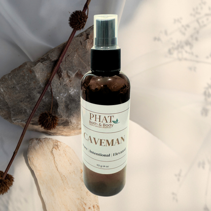 Bottle of 'Caveman' spray from Phat Bath & Body on a neutral background with decorative elements.