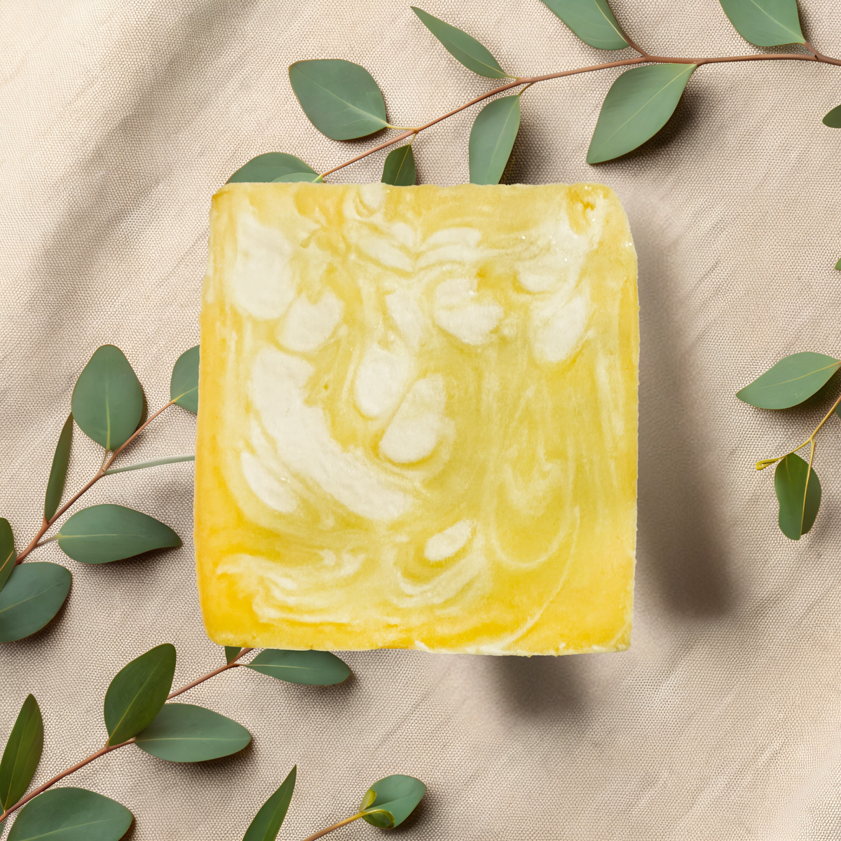 Marbled yellow and white soap bar on a beige fabric background with green leaves.