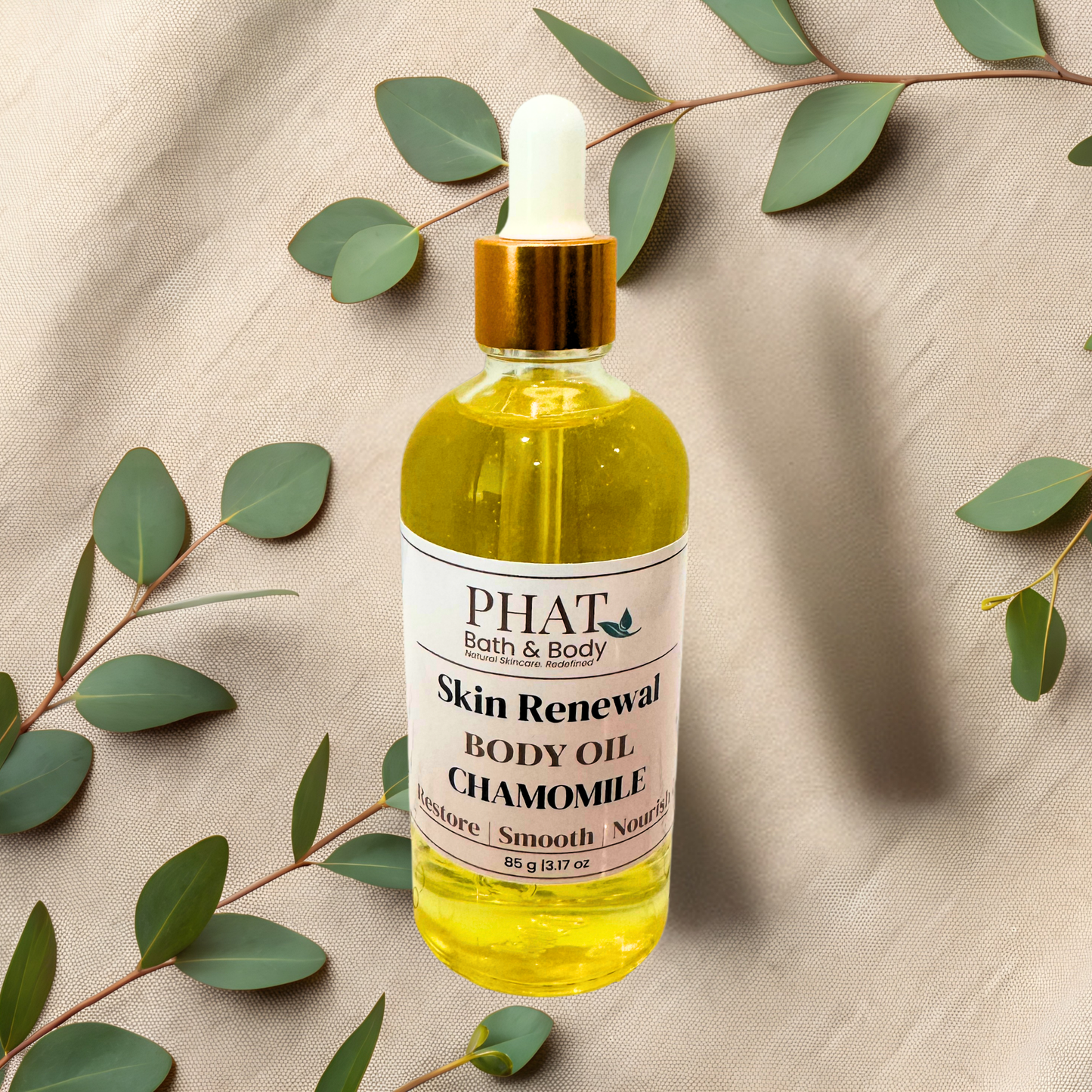 Bottle of PHAT Bath & Body Skin Renewal Body Oil with Chamomile on a beige fabric background with green leaves.