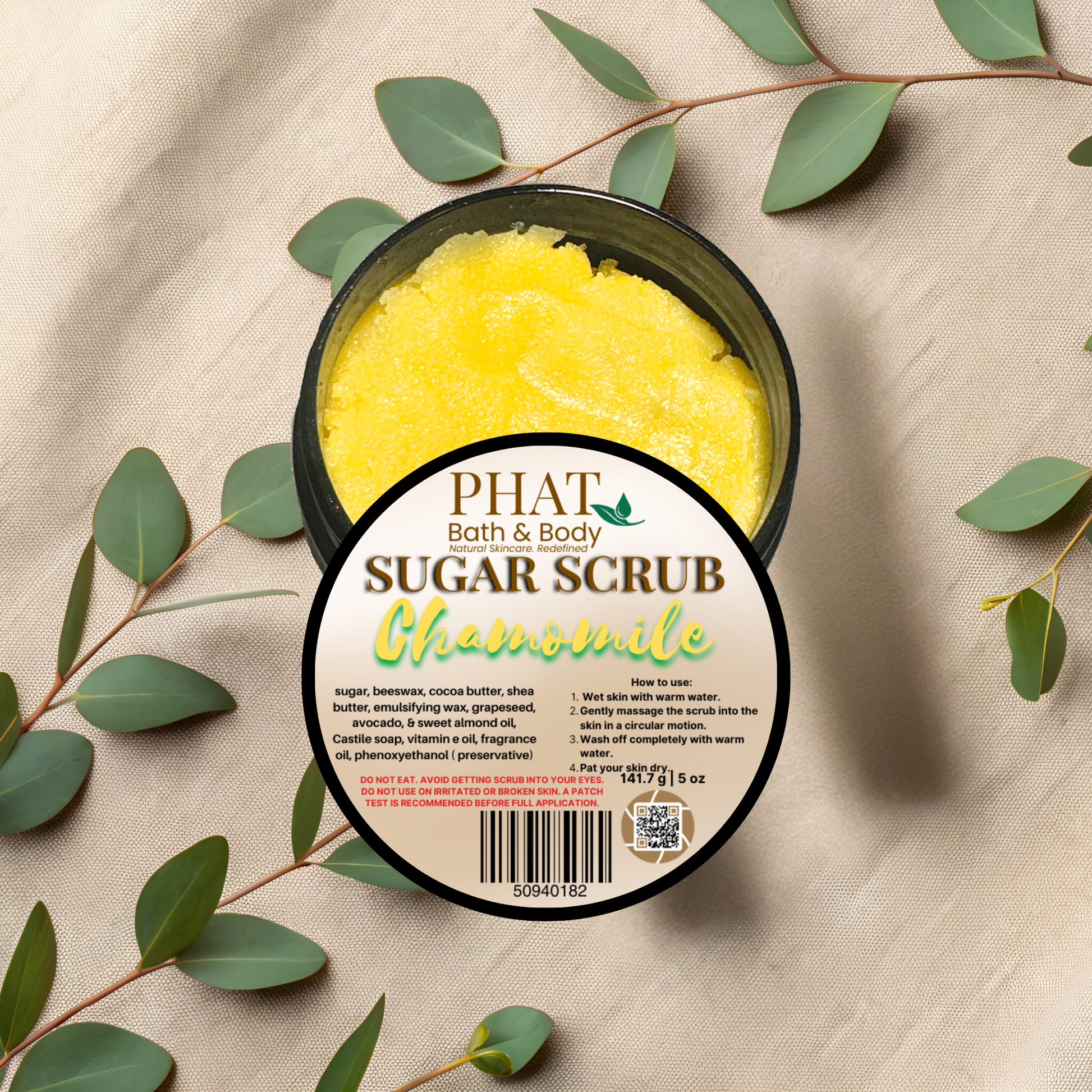 Jar of Phat Bath & Body Chamomile Sugar Scrub with green leaves on a beige fabric background