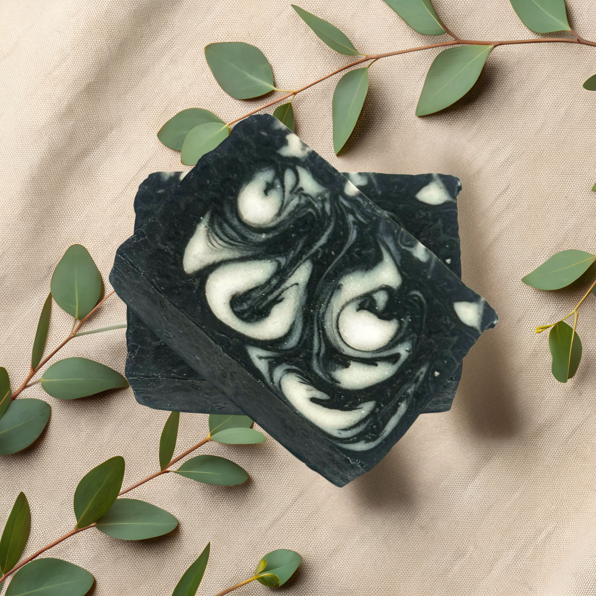 Black and white swirled soap bar on a beige fabric background with green leaves.