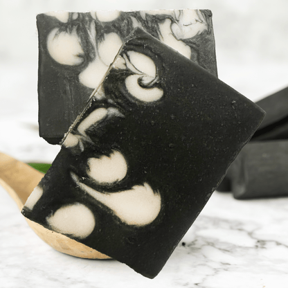 Black and white marbled soap bars on a marble surface with a wooden spoon.