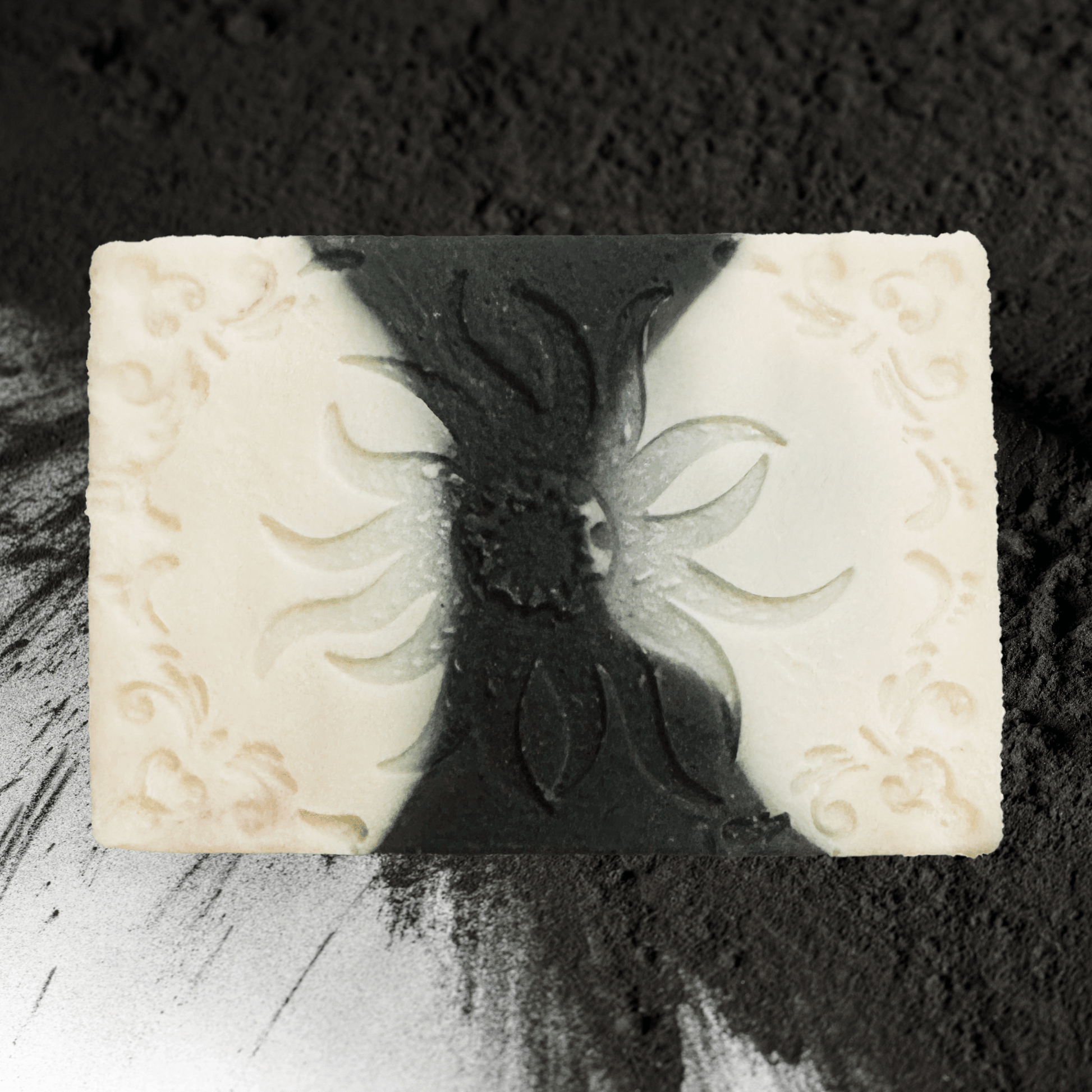 Decorative charcoal soap bar with embossed design on a textured black background