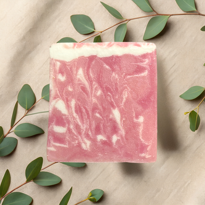 Pink soap bar with white swirls on a beige fabric background with green leaves.