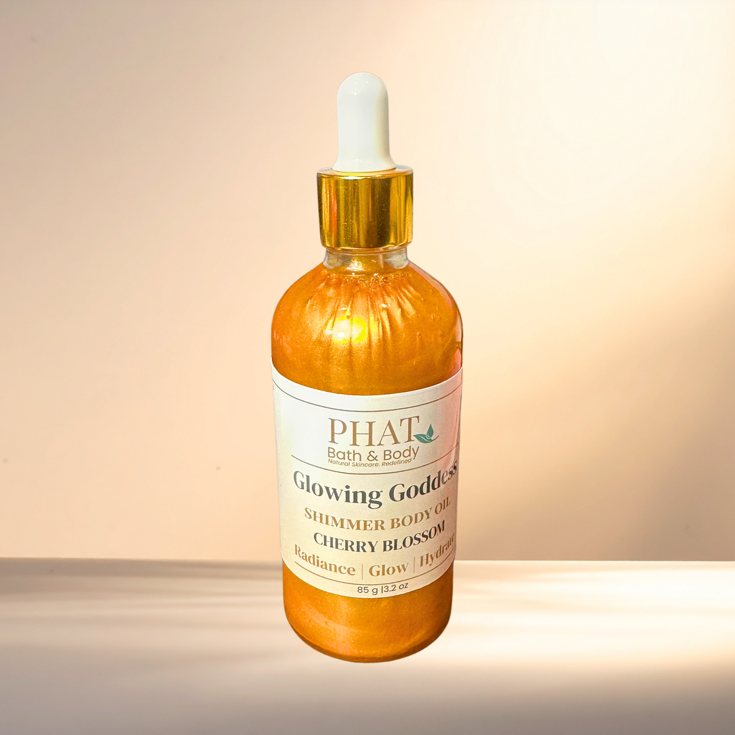 Bottle of 'Glowing Goddess' shimmer body oil by PHAT Bath & Body on a gradient background