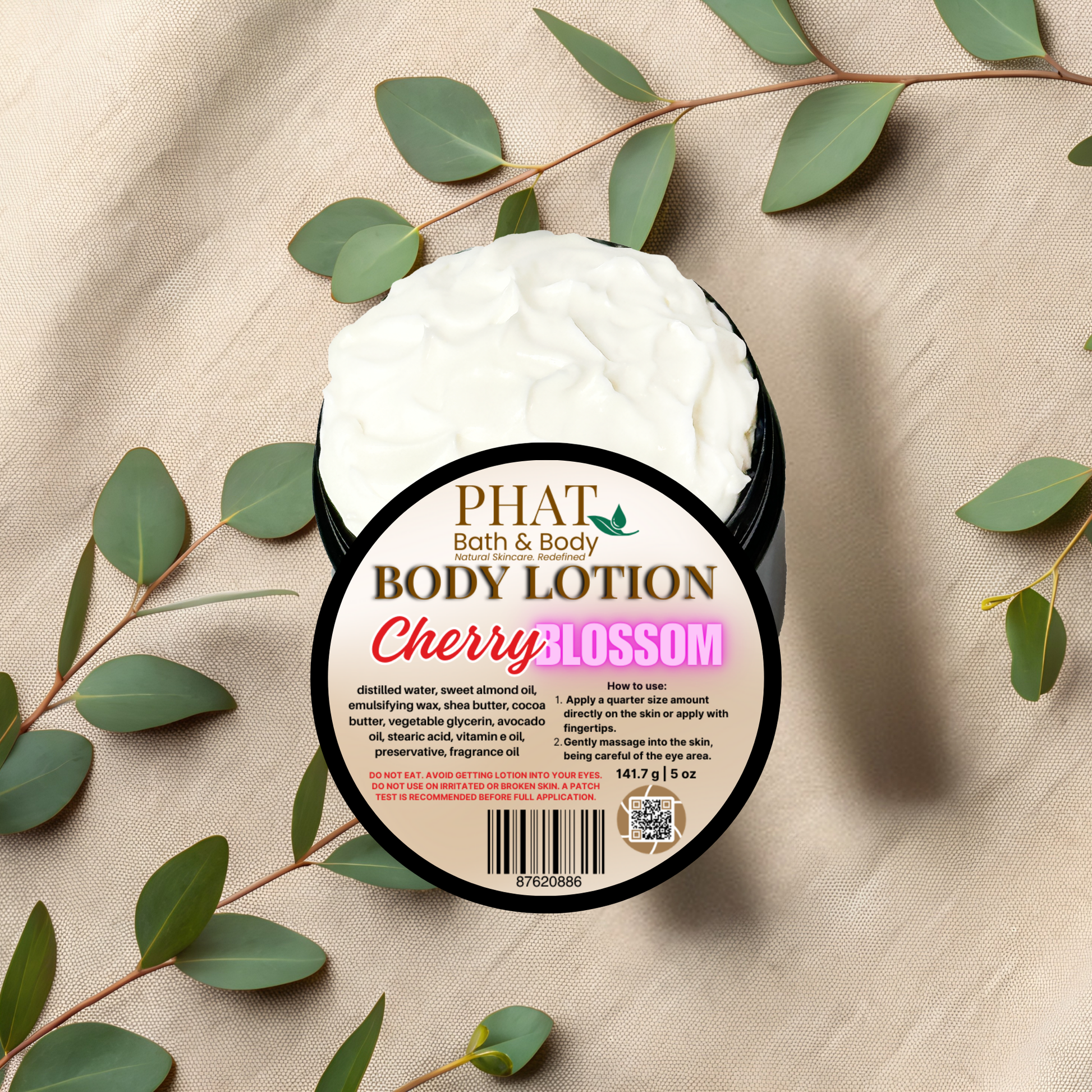 Body lotion container labeled 'Cherry Blossom' by Phat Bath & Body on a beige fabric background with green leaves.