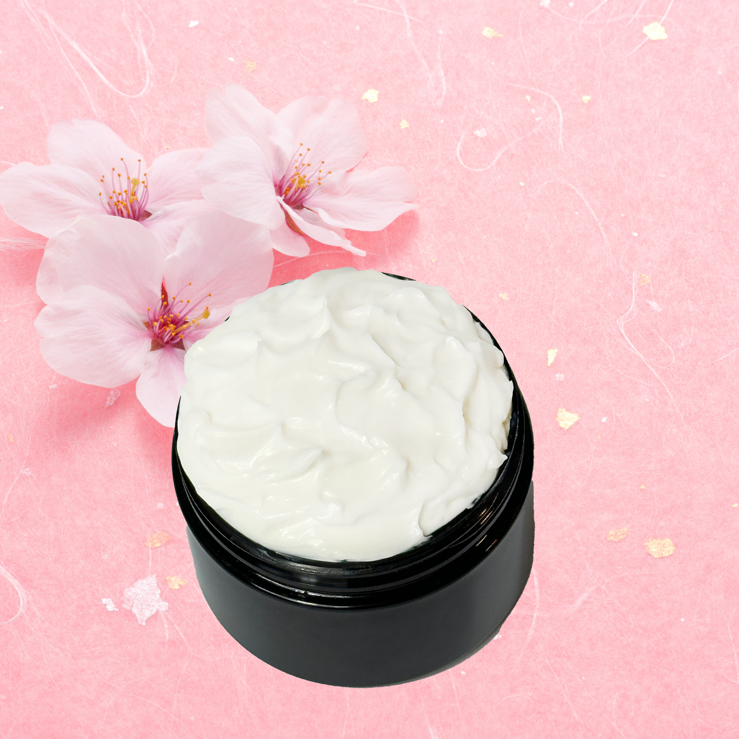 Black jar of white body cream with cherry blossoms on a pink background