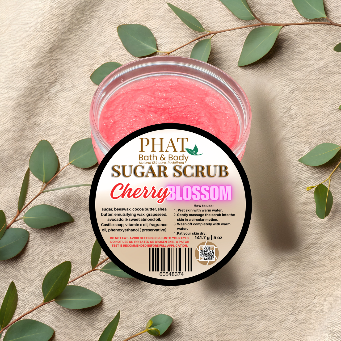Jar of cherry blossom sugar scrub with a label on a beige fabric background with green leaves.