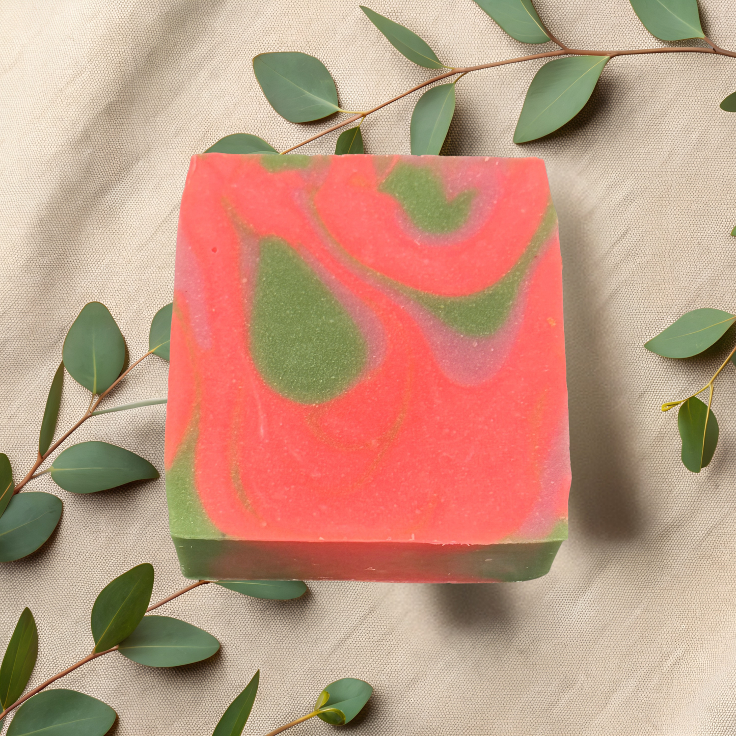 Bar of pink and green soap with eucalyptus leaves on a beige fabric background