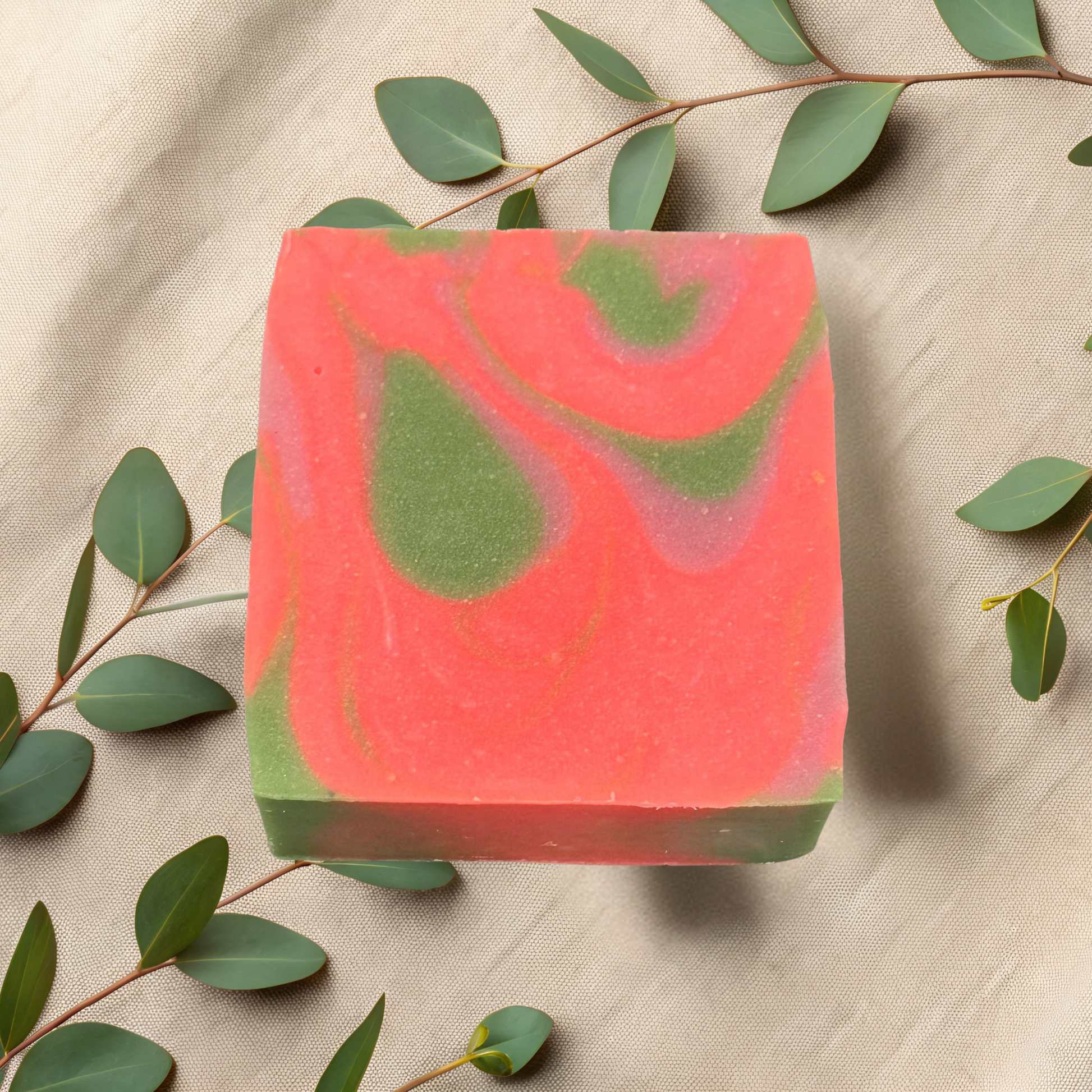 Bar of pink and green soap with eucalyptus leaves on a beige fabric background