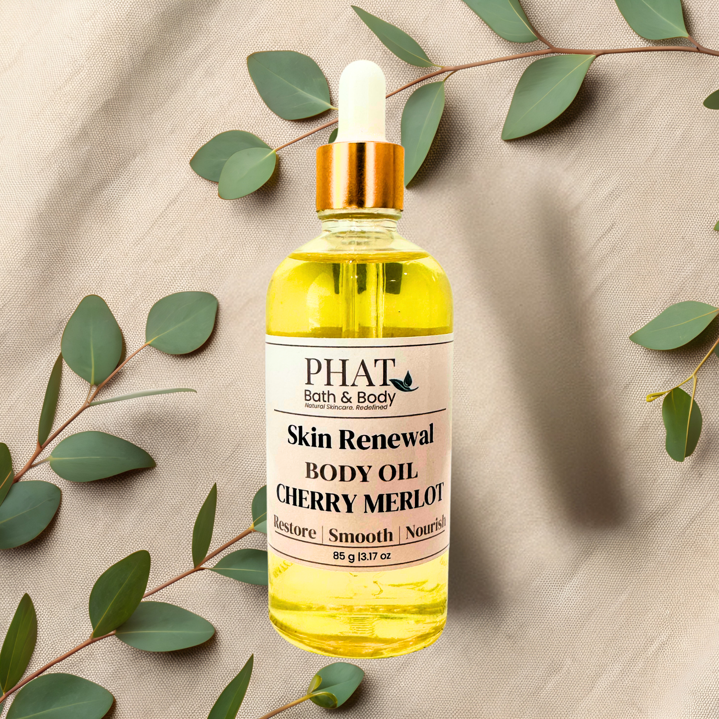 Bottle of body oil from PHAT Bath & Body on a beige fabric background with green leaves.