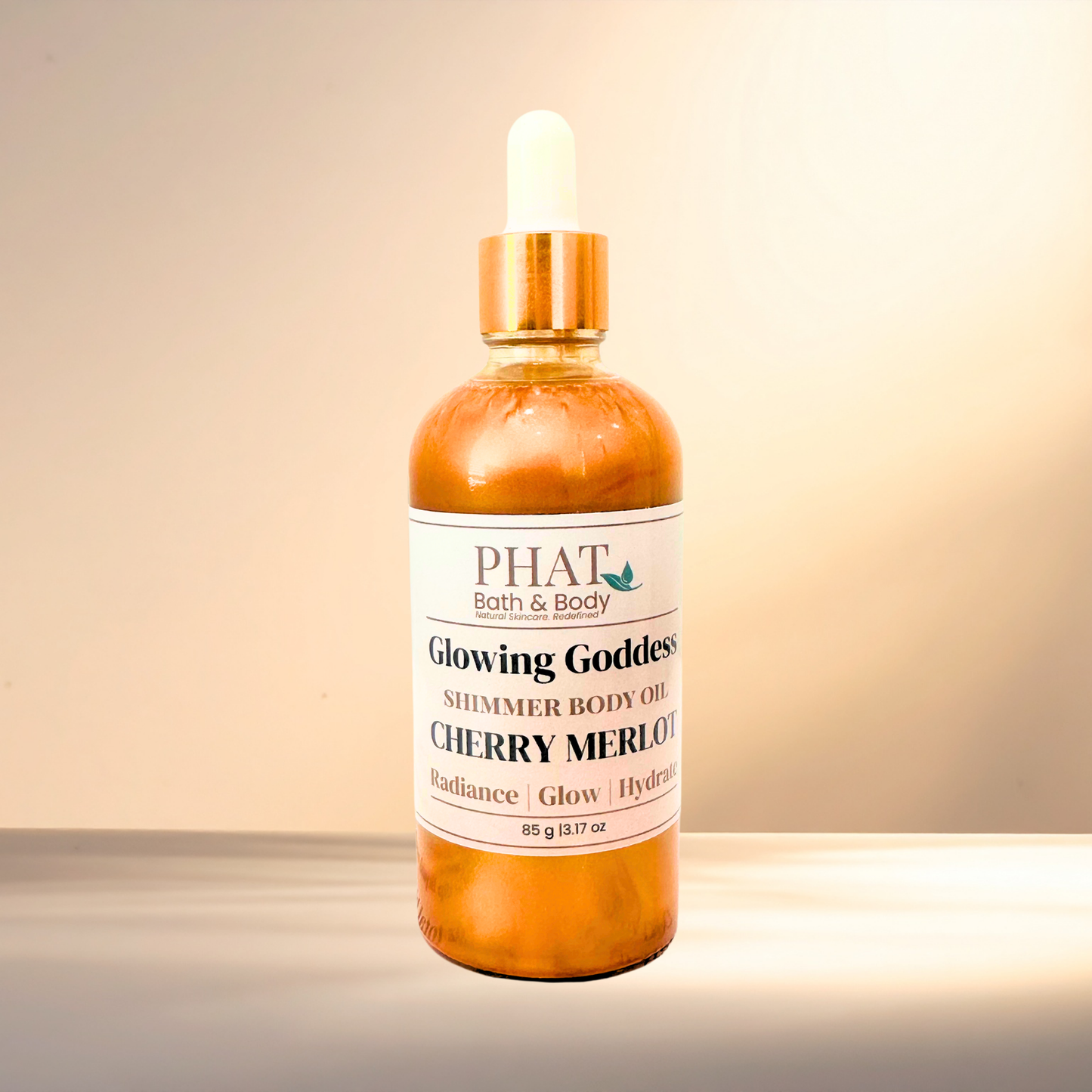 Bottle of 'Glowing Goddess' shimmer body oil by PHAT Bath & Body on a gradient background