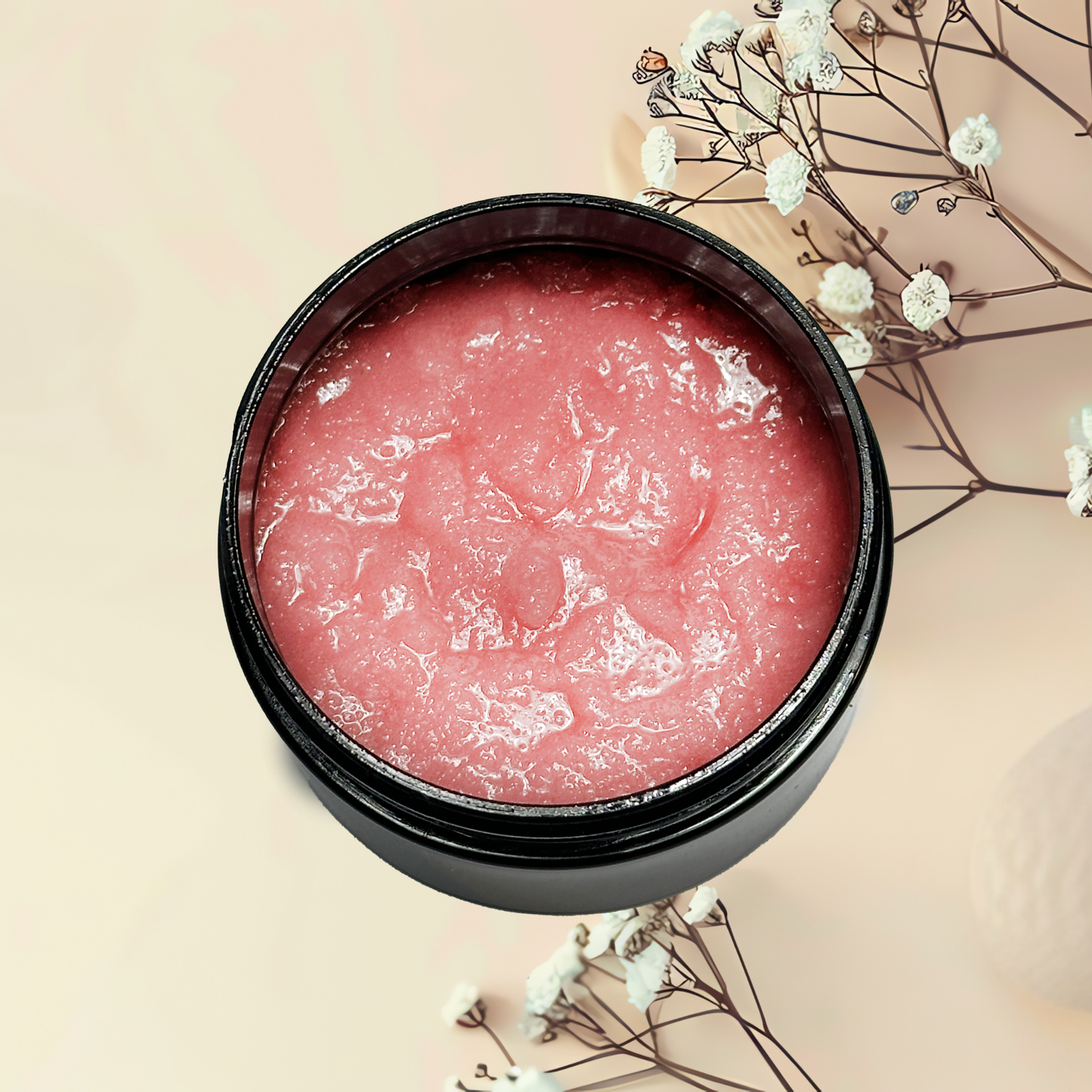 Pink scrub product in a black container with white flowers on a beige background