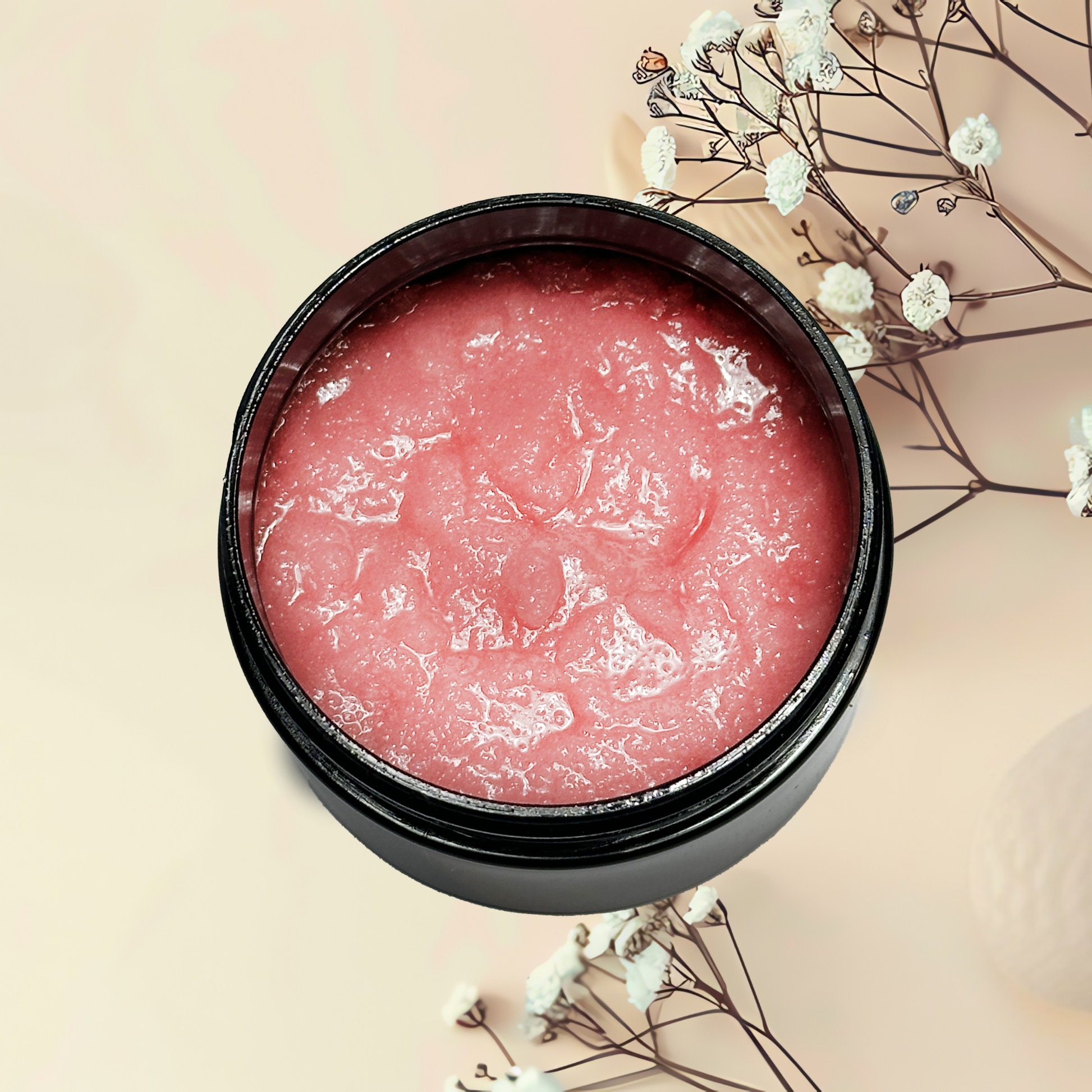 Pink scrub product in a black container with white flowers on a beige background