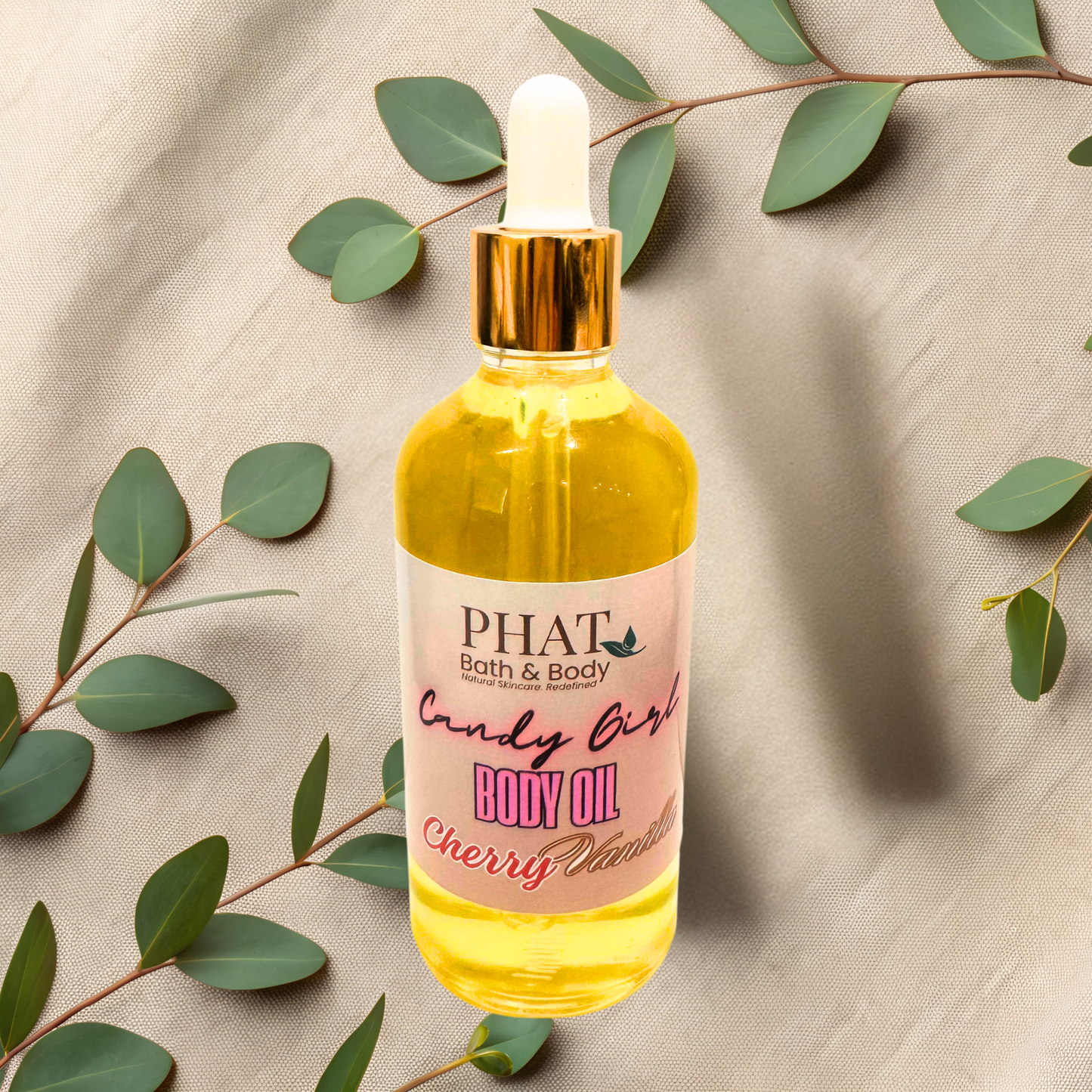 Body oil bottle labeled 'Candy Girl' by PHAT Bath & Body on a beige fabric background with green leaves.