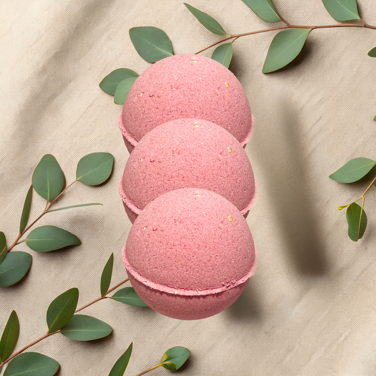 Three pink bath bombs with green leaves on a beige fabric background