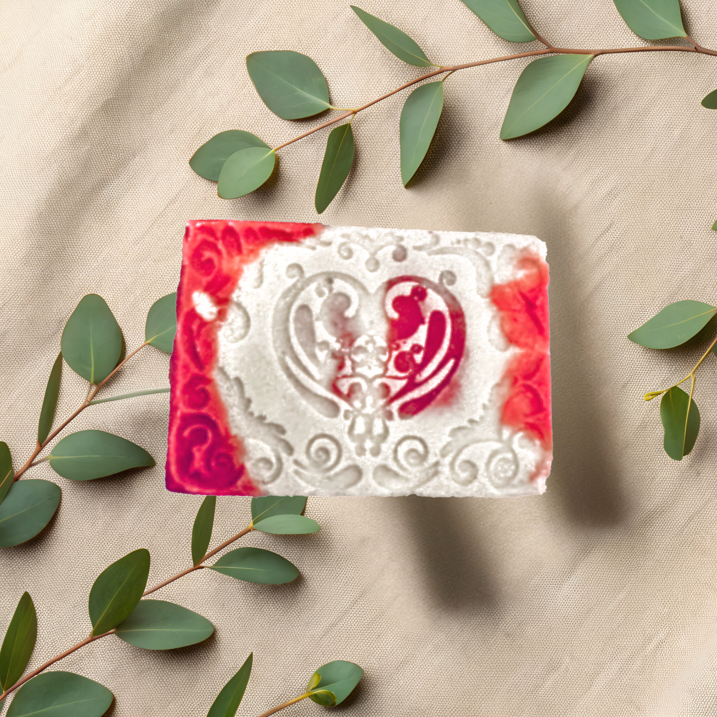 Decorative soap bar with red and white design on a beige fabric background with green leaves.