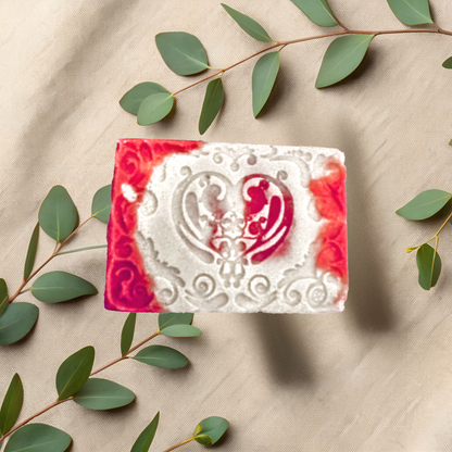 Decorative soap bar with red and white design on a beige fabric background with green leaves.