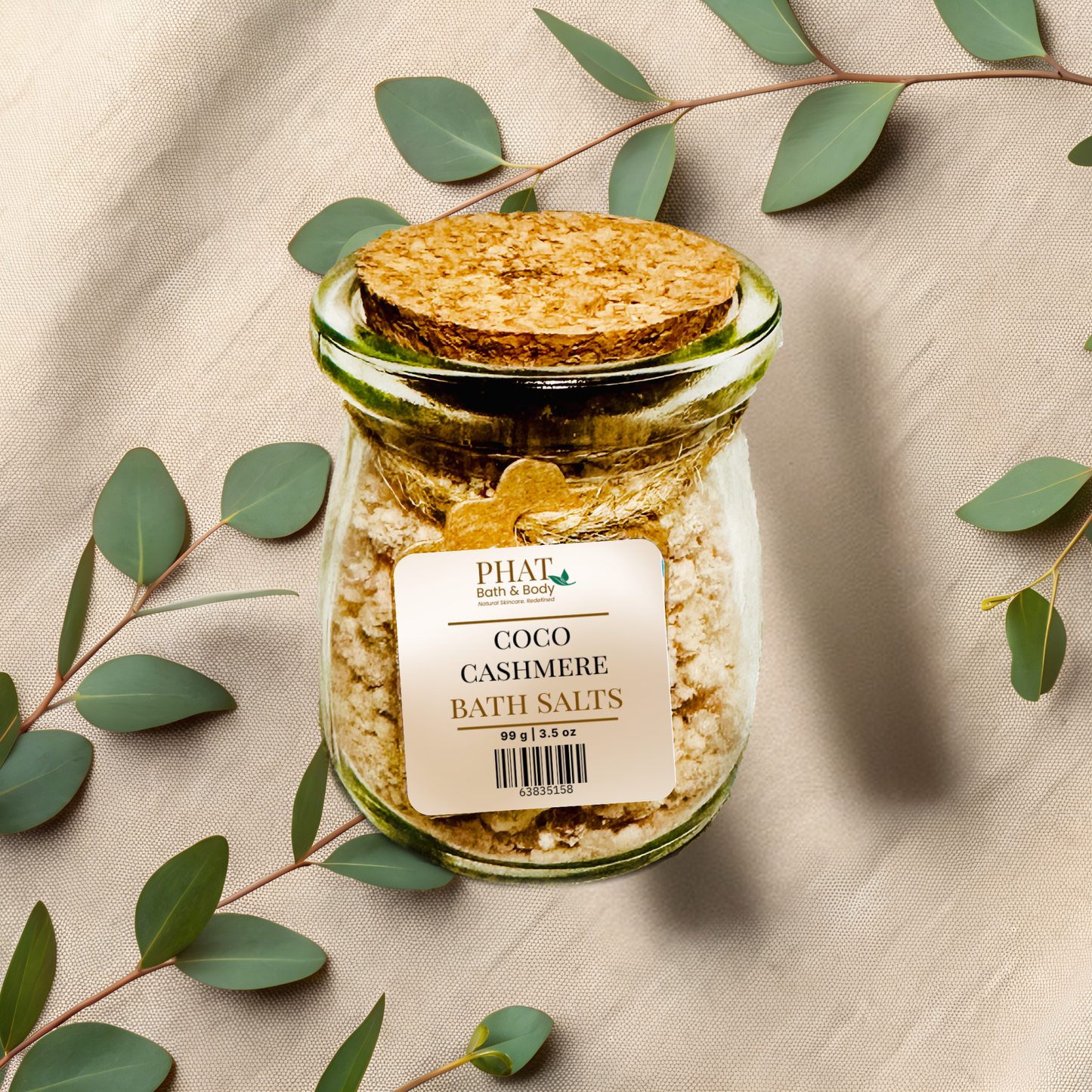 Jar of coco cashmere bath salts with a decorative label on a beige fabric background with eucalyptus leaves.