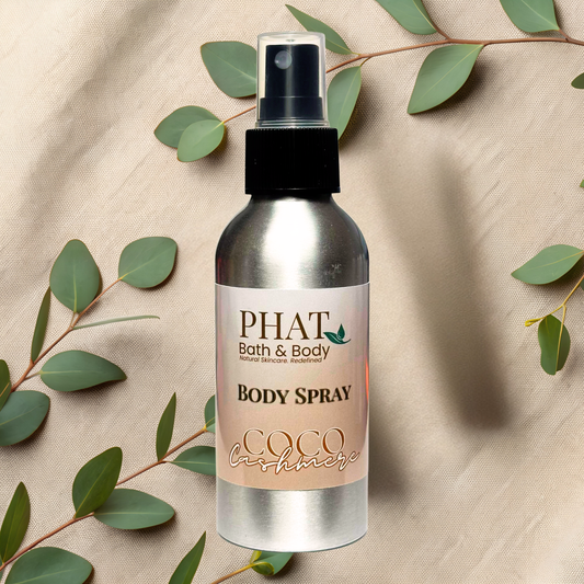 Body spray bottle with 'PHAT Bath & Body' label on a beige fabric background with green leaves.