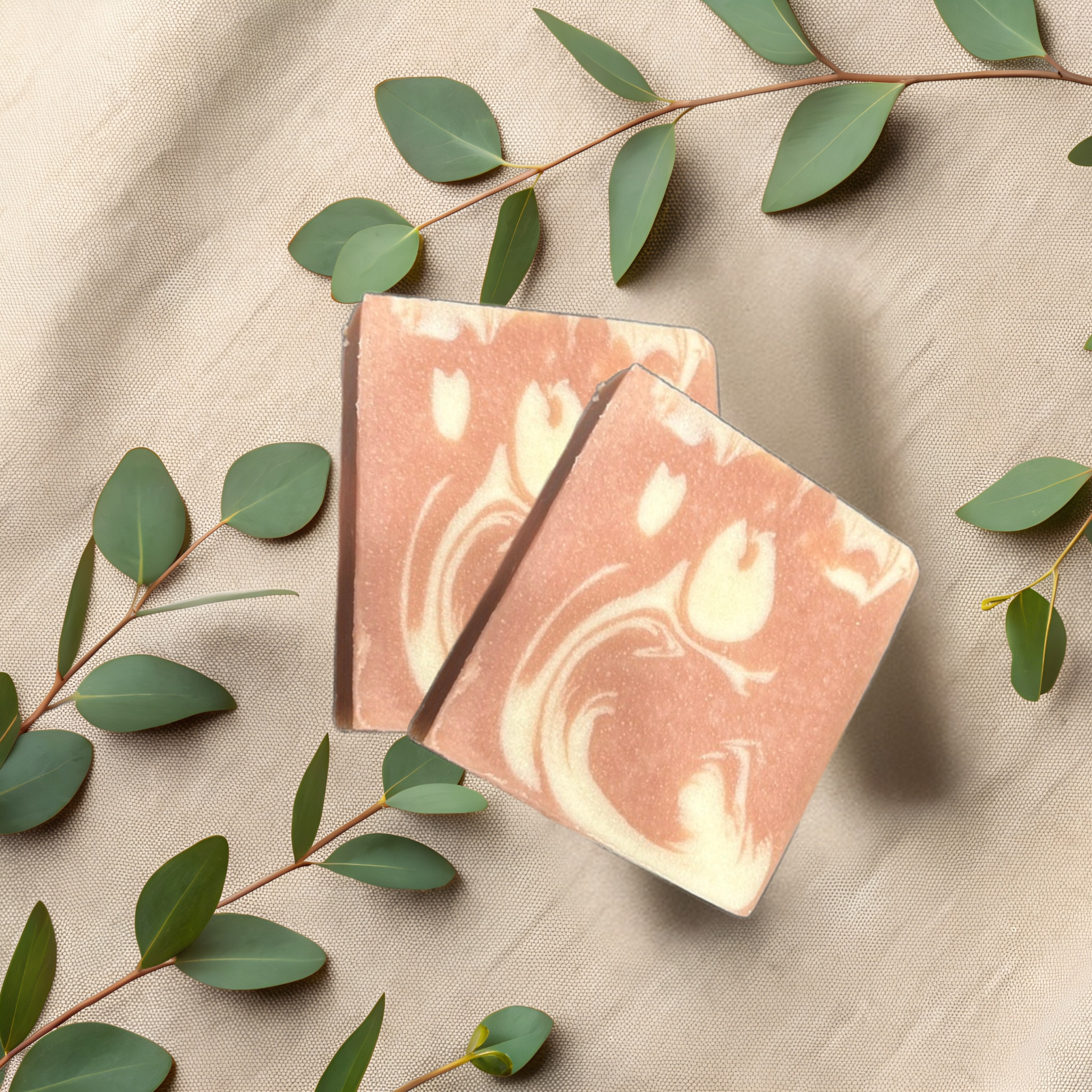 Two marbled brown and white soap bars on a beige fabric background with green leaves.