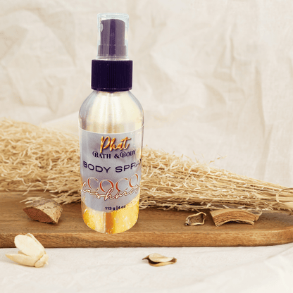 Body spray bottle labeled 'Phat Bath & Body' with 'Coco Cashmere' on a wooden board with dried plants.