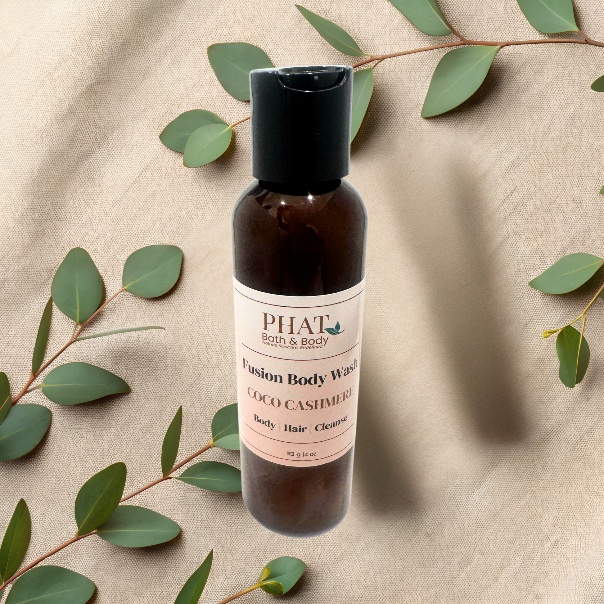 Bottle of PHAT Bath & Body Fusion Body Wash with eucalyptus leaves on a beige fabric background