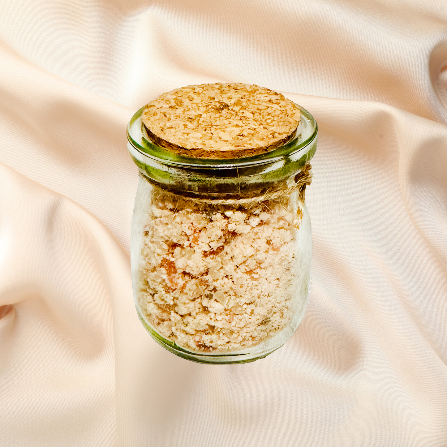 Small glass jar with beige bath salt on a beige fabric background