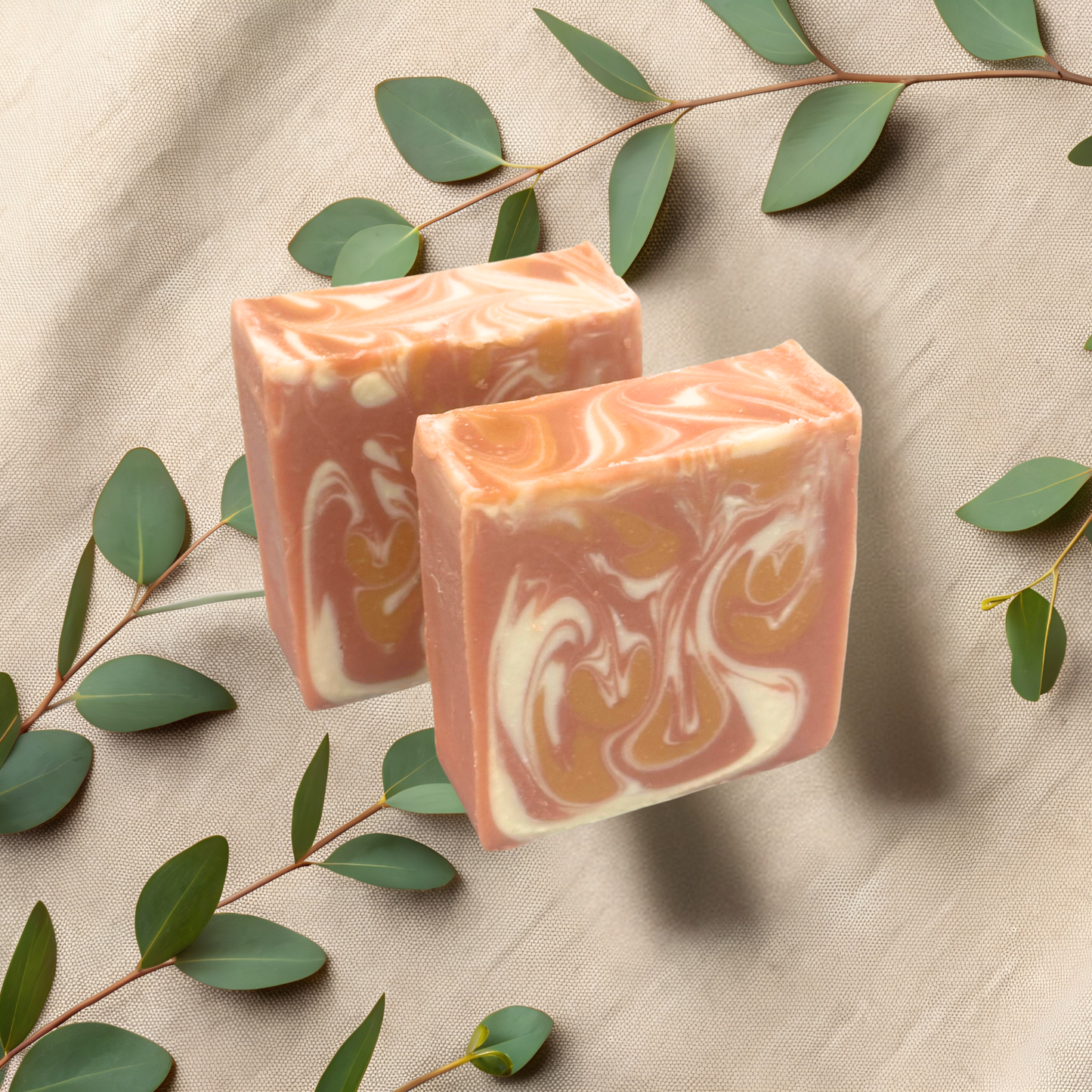 Two bars of soap  on a beige fabric background with green leaves.