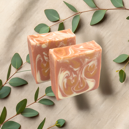 Two bars of soap  on a beige fabric background with green leaves.