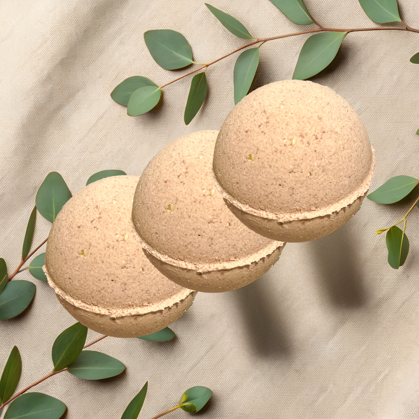 Three beige bath bombs with green leaves on a beige fabric background