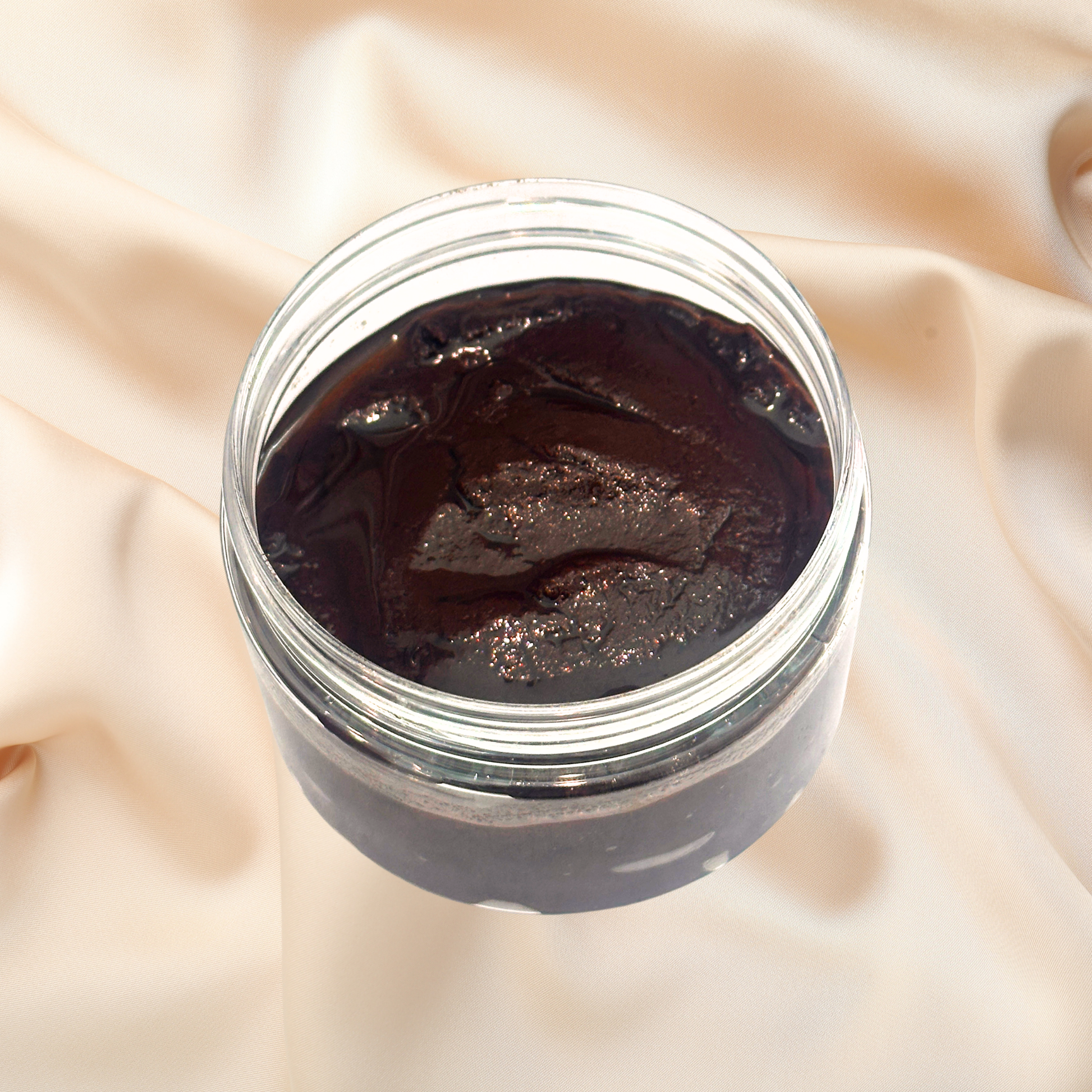 Jar of dark brown scrub on a beige fabric background
