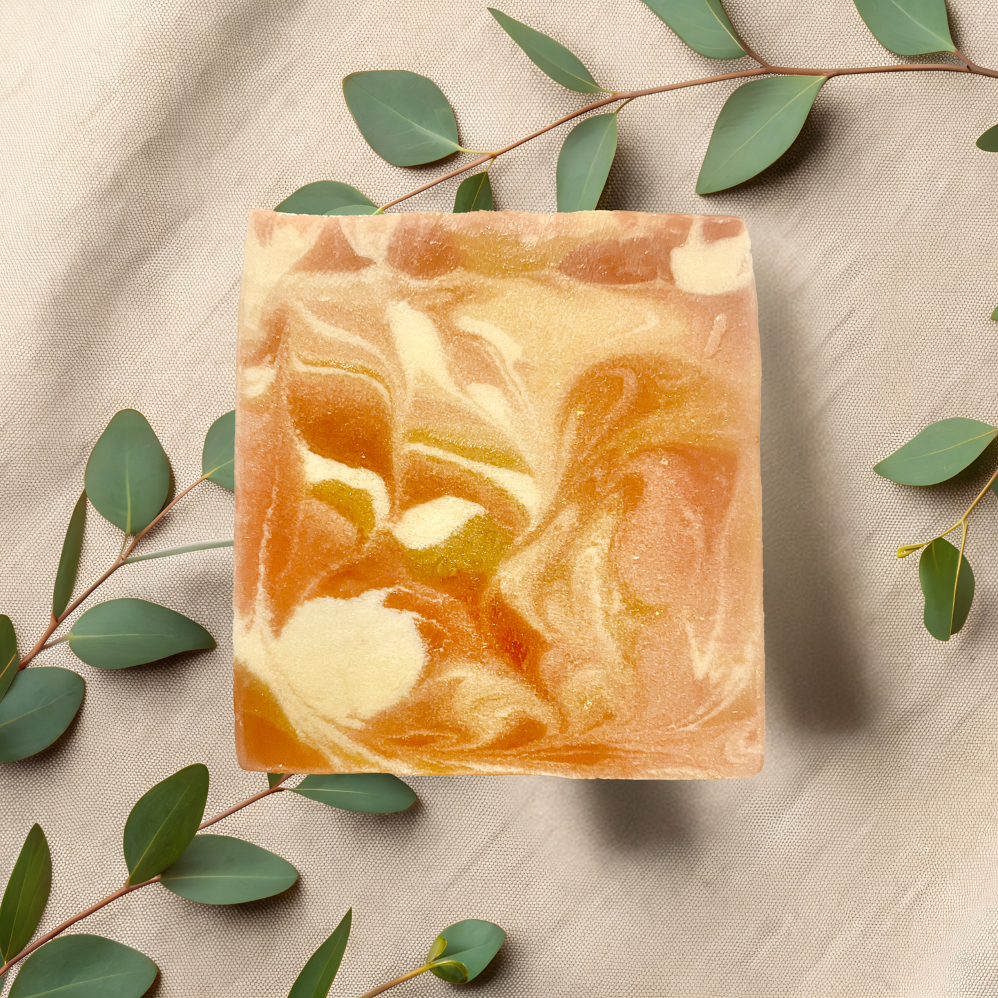 Marbled soap bar with green leaves on a beige fabric background