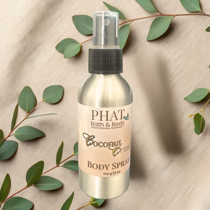 Body spray bottle labeled 'Coconut Cream' from PHAT Bath & Body on a beige fabric background with green leaves.