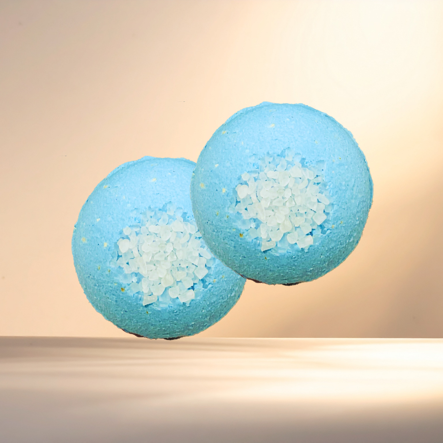 Two blue bath bombs with visible sea salt on a beige background