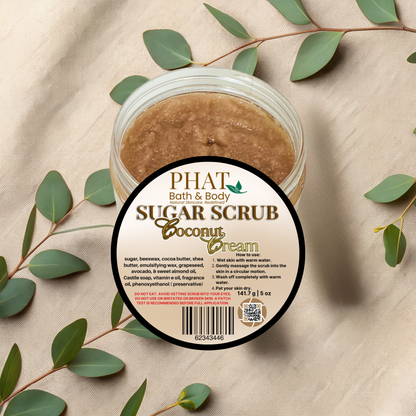 Jar of Phat Bath & Body Sugar Scrub Coconut Cream with green leaves on a beige fabric background