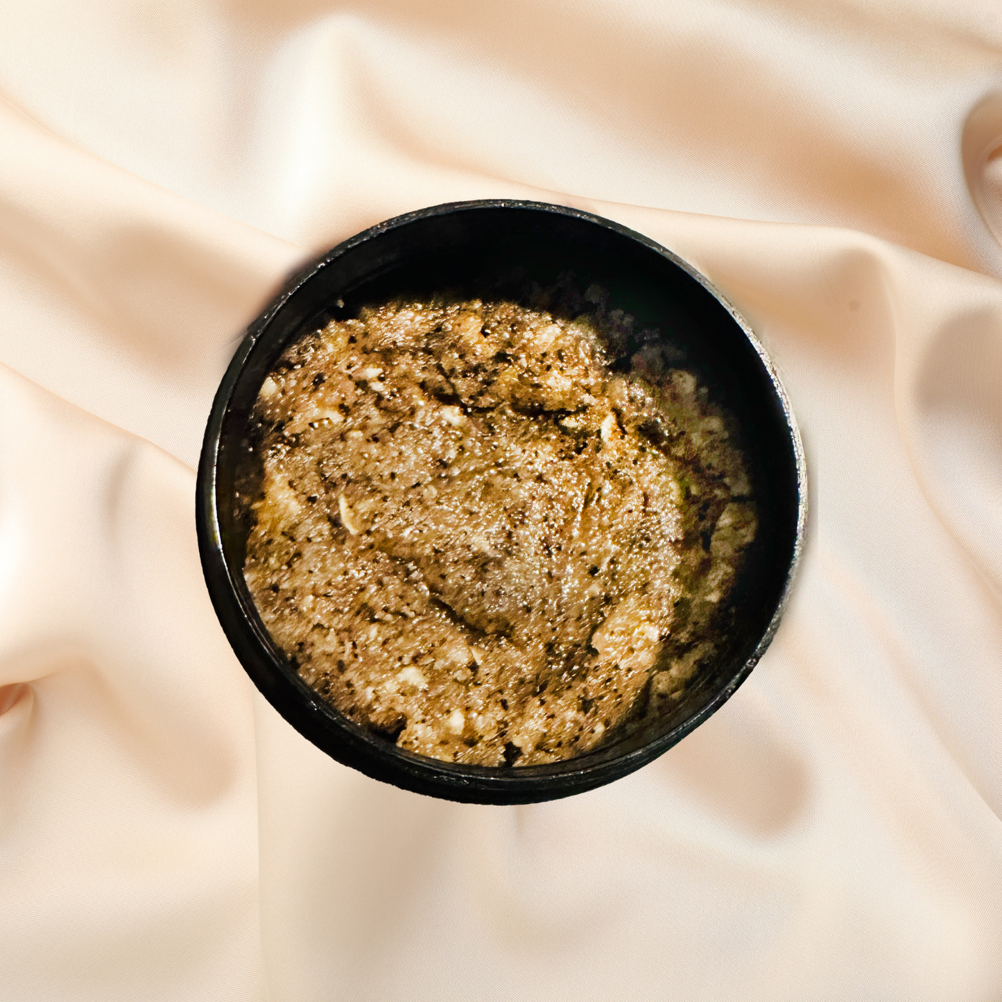 Black container of brown sugar scrub on a beige fabric background