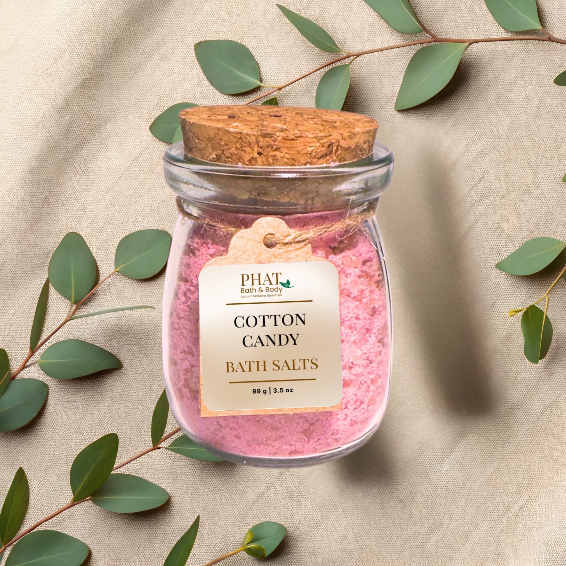 Jar of Cotton Candy Bath Salts with a cork lid on a beige fabric background with eucalyptus leaves.